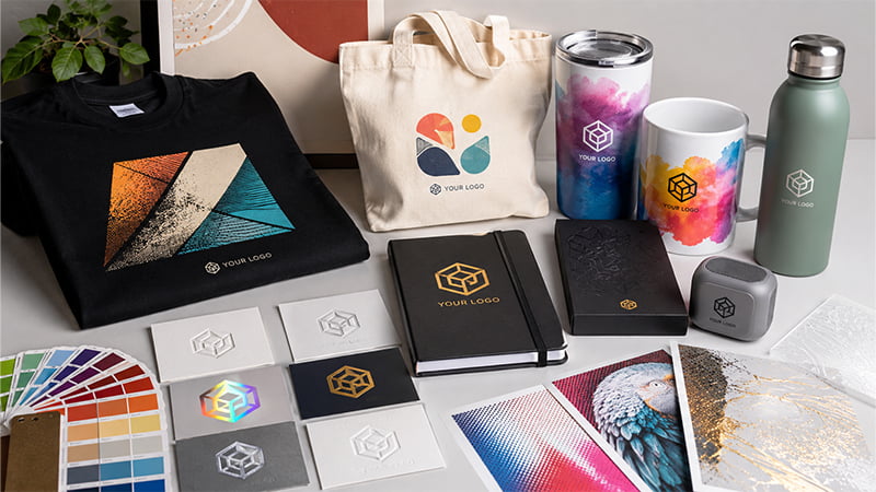 Custom branded products showing different printing and decoration methods on apparel bags drinkware notebooks cards and packaging