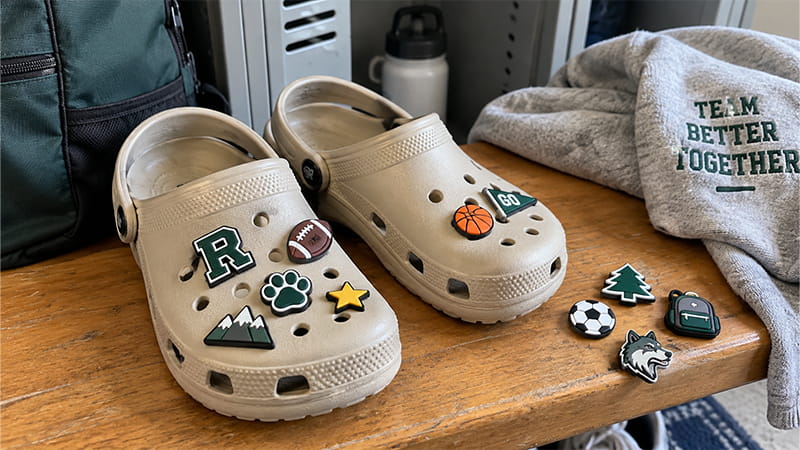 Custom shoe charms arranged on clogs, including a letter, paw print, football, star, mountain, and other interchangeable icons.