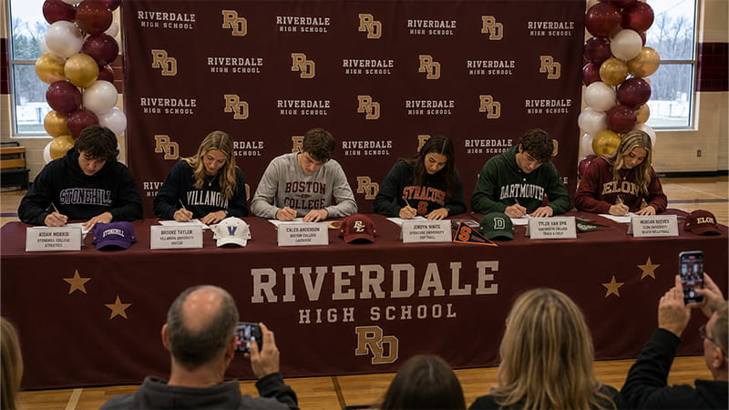 Separate nameplates, documents, and college hats give six athletes their own space at one shared table