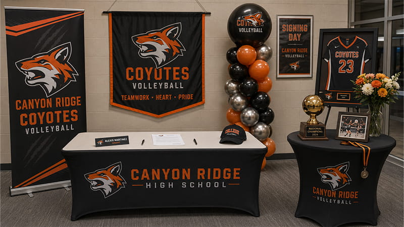 Signing table framed by vertical banners, balloons, a jersey, flowers, and a trophy display