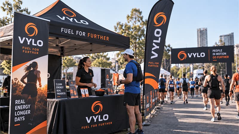 Outdoor vendor booth using tall feather flags and overhead canopy branding to raise the main message above the table.